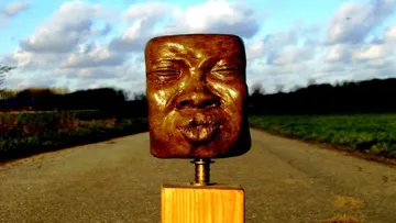 Bronze face sculpture on a rural road.