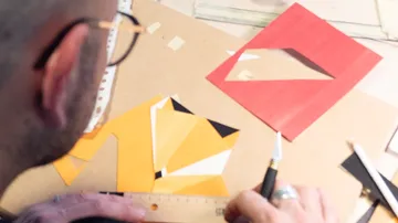 Person gestaltet geometrische Papierkunst auf Tisch.