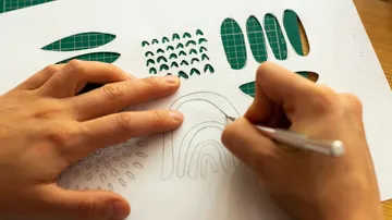 Person cutting patterns on paper with knife.