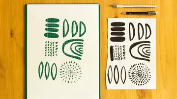 Schablone und Papier mit abstrakten Mustern auf Tisch.