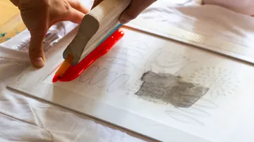 Holzrakel drückt Farbe auf Papier.