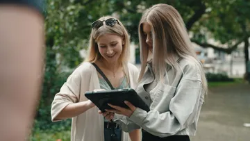 Zwei Frauen betrachten ein Tablet draußen.