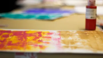 Paintbrush on canvas with colorful strokes.