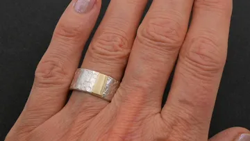 Hand trägt einen strukturierten Silberring.