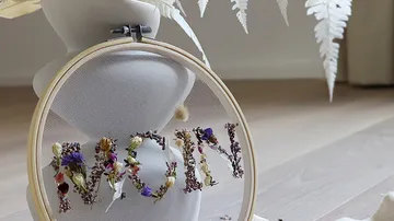 Embroidered hoop spelling 'MOM' with flowers indoors.