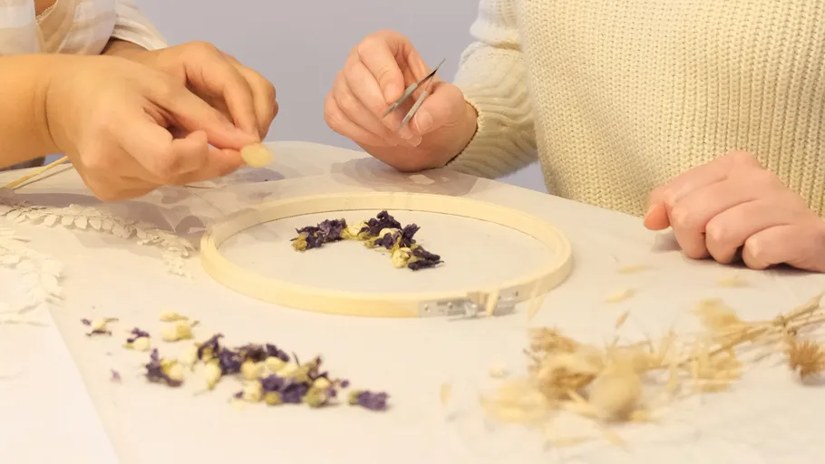 Hands arranging flowers in embroidery hoop.