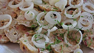 Sliced meat dish with onions and herbs.
