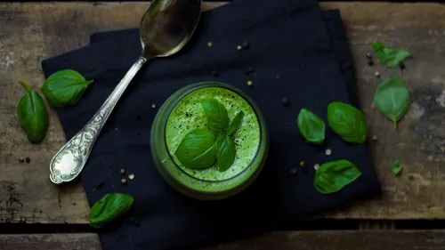 Green smoothie with basil leaves on table.