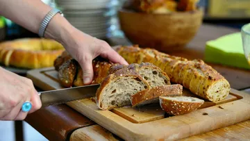Person slicing bread on wooden board.
