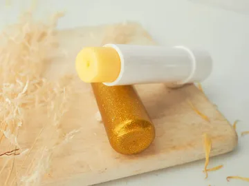 Gold-colored lip balm sits next to a white pencil.