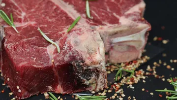 Raw steak with herbs and spices on black surface.