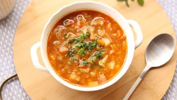 Soup in white bowl on wooden board.