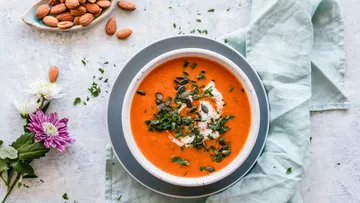 Tomatensuppe mit Kräutern und Samen auf Tisch.