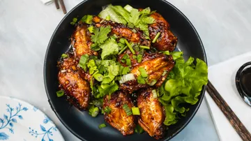 Spicy chicken wings with herbs in black bowl.