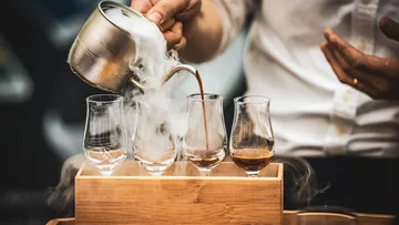 Hand pours liquid into misty glasses on wood.