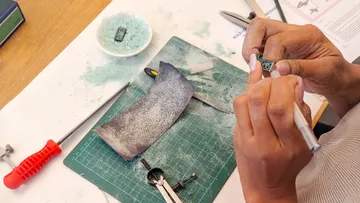 Hands crafting jewelry model on a mat.