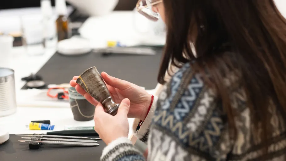 Person examining silver cup at table.