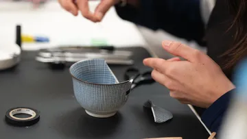 Person repariert kaputte Tasse auf Tisch.