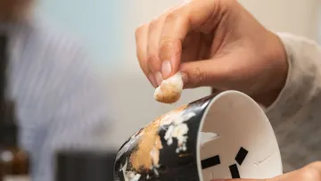 Hand trägt Substanz auf gesprungene Schale auf.