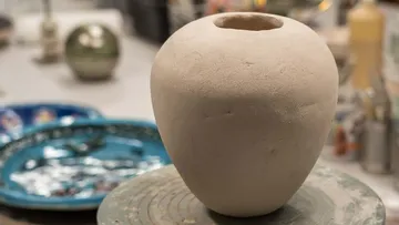 Unfinished clay vase on pottery wheel, workshop setting.