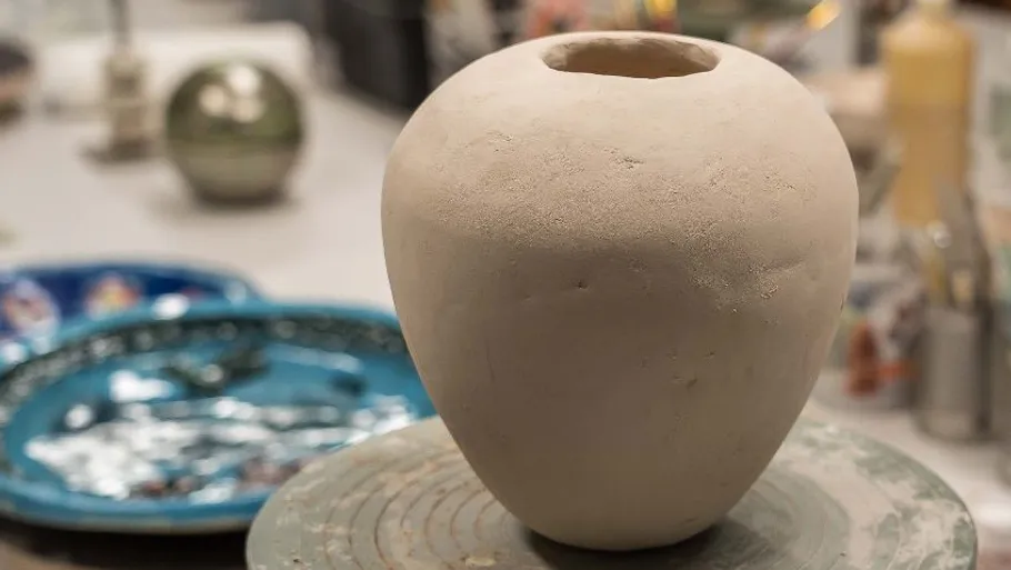 Unfinished clay vase on pottery wheel, workshop setting.