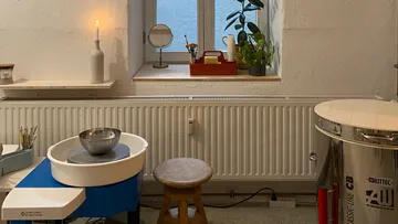 Pottery studio with wheel and stool, window above.