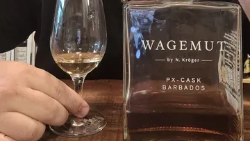 Hand holds glass next to Wagemut bottle.