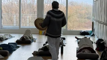 Person trommelt im Yoga-Studio mit Teilnehmern.