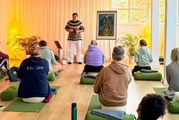 Group meditating with instructor in a bright room.