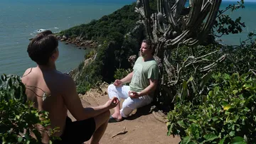 Two men meditating on a cliff edge.