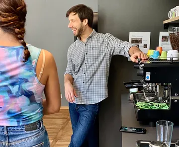 Mann lächelnd neben Kaffeemaschine im Café.
