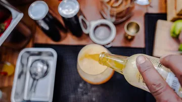 Hand gießt Getränk ins Glas an Bar.