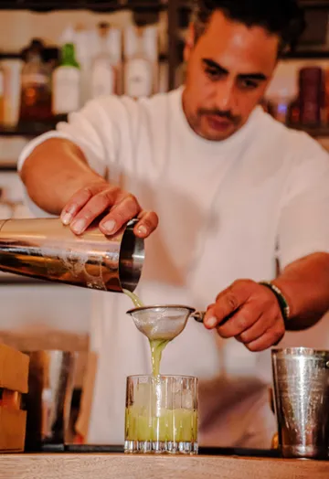 Bartender pouring green drink through strainer.