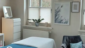 Gemütlicher Massageraum mit Bett und Stuhl.