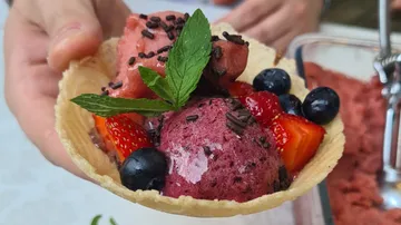 Hand holds berry sorbet in waffle bowl.