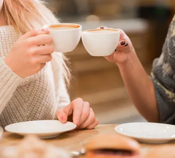 Two people clinking coffee cups indoors.