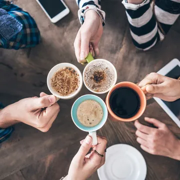 Four hands holding coffee cups together.
