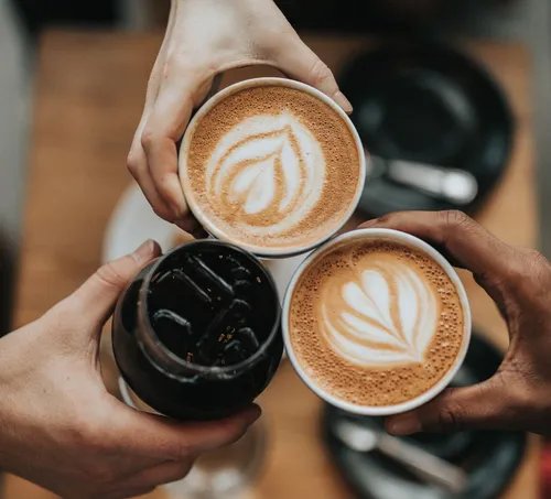 Drei Hände halten Kaffee und Kaltgetränk.
