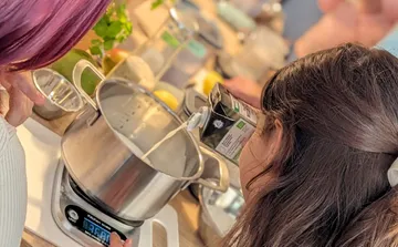 Person pouring liquid into pot on stove.