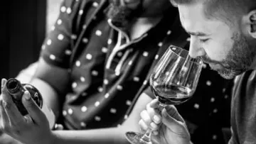 Man smelling wine, another examining bottle.