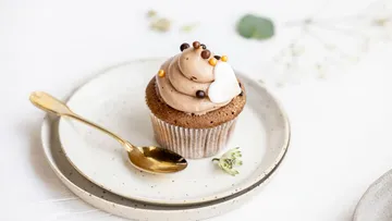 Cupcake mit Frosting auf weißem Teller, goldener Löffel.