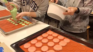 Two people making colorful macarons in kitchen.