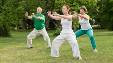Drei Personen machen Tai Chi im Park.