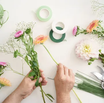 Hände arrangieren Blumen auf einem weißen Tisch.