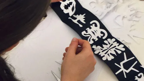 Person arranging paper cutouts on black background.