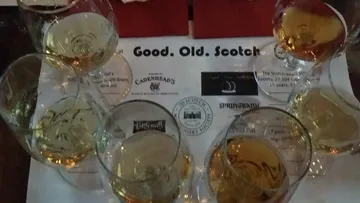 Sechs Whiskygläser auf einer bedruckten Matte.