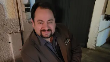 Mann lächelt drinnen, sitzt an der Wand.