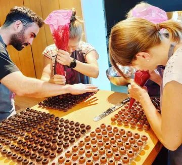 Personen füllen Schokoladenformen mit roten Spritzbeuteln.