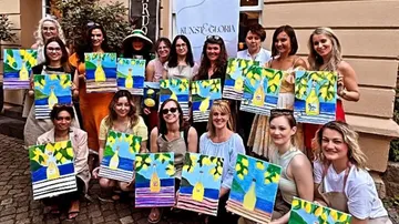 Group holding colorful paintings outdoors.