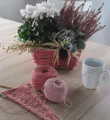 Basket with flowers, yarn, and mug on table.